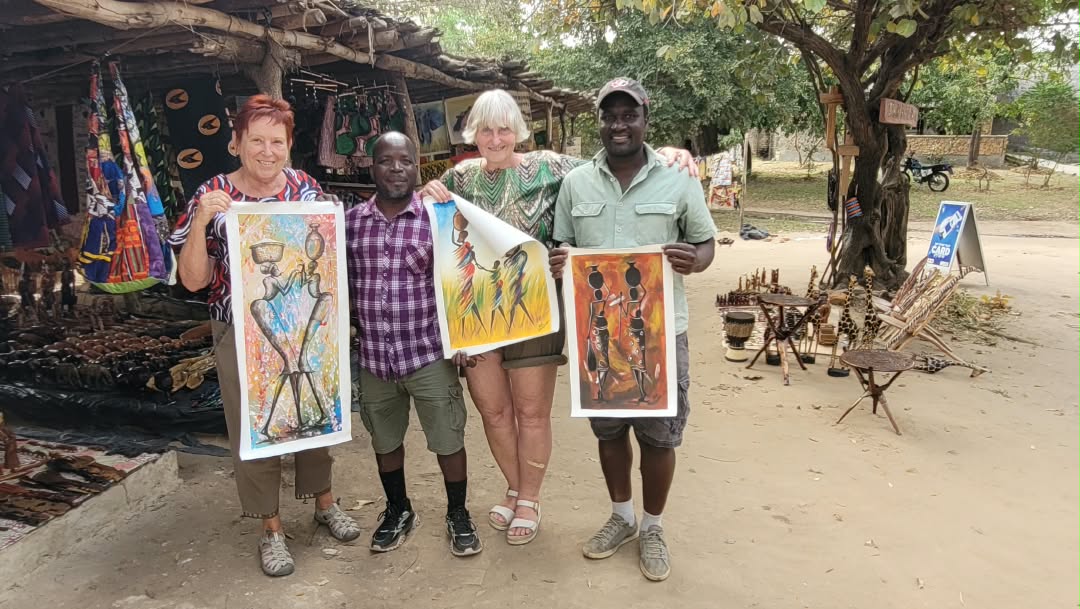 William and travellers holding hand-painted African artwork at a craft market
